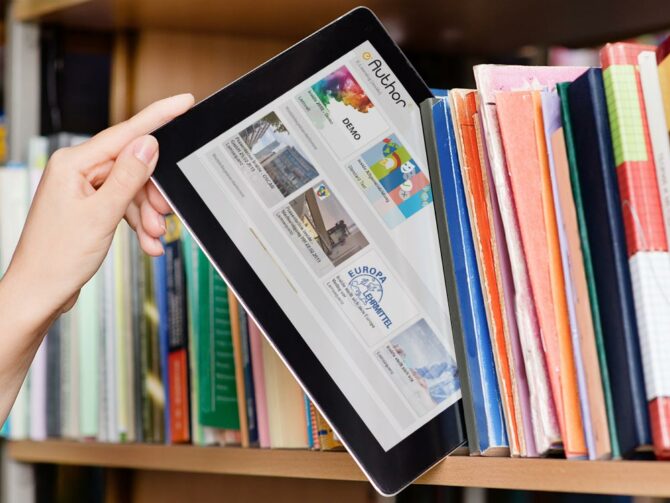 Eine Hand nimmt ein Tablet mit dem Autorensystem eAuthor auf dem Bildschirm aus einem Bücherregal